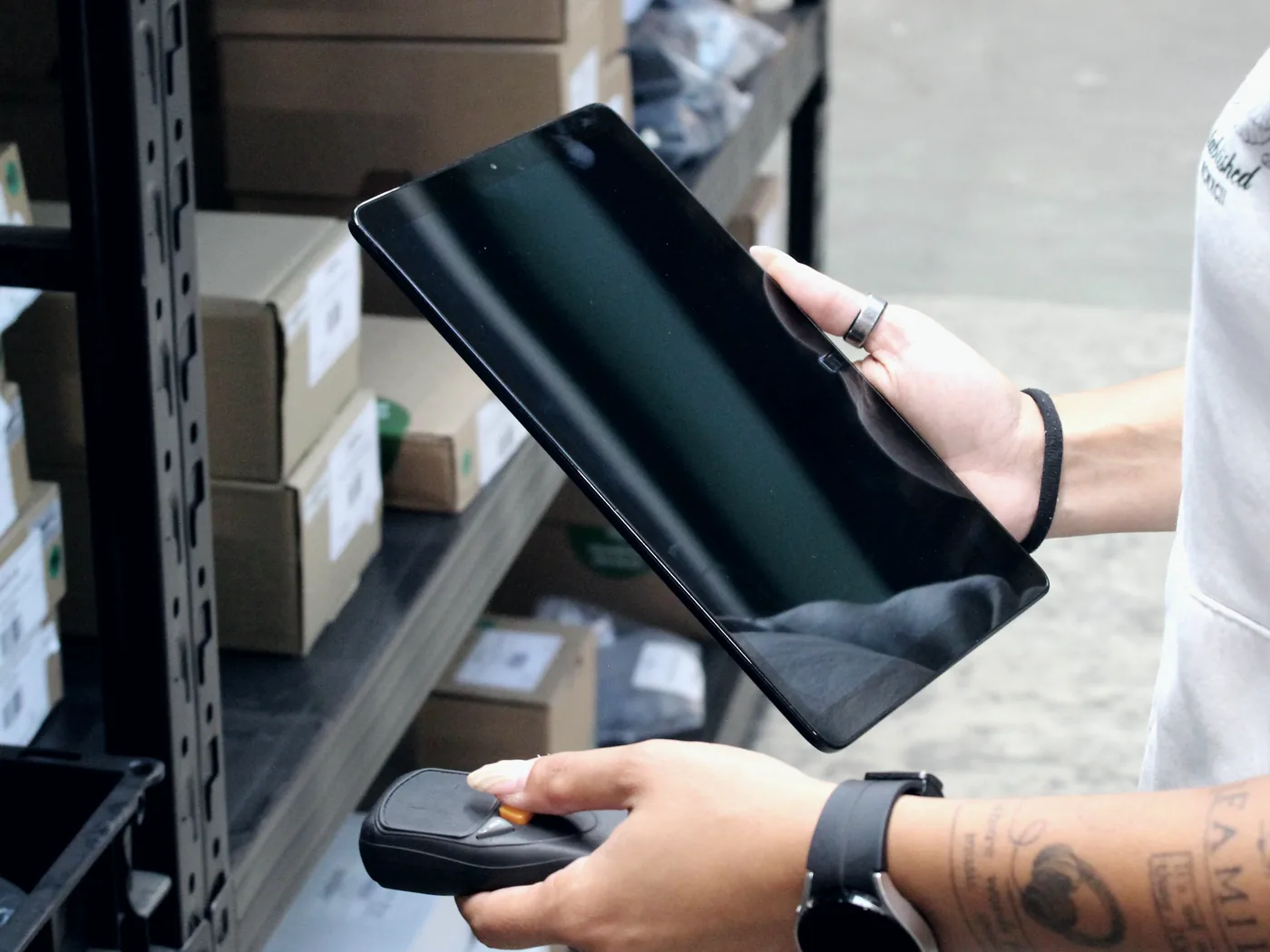 Mitarbeiterin erfasst Lagerware mit Handscanner und Tablet am Fachbodenregal – Bestandsführung im Lager der PS Produktion-Service GmbH