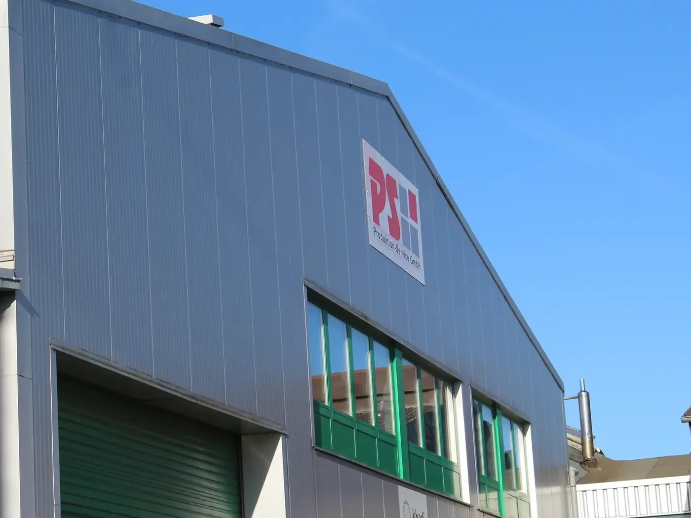 Lagerhalle der PS Produktion-Service GmbH mit Firmenschild an der Fassade und geschlossenem Verladetor